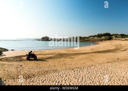 Mann sitzt auf einem ATV an einem Strand mit dem Meer im Hintergrund Stockfoto