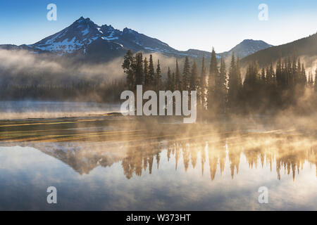 South Sister und Broken Top spiegeln sich in den ruhigen Gewässern des Sparks Lake bei Sonnenaufgang in der Cascades Range in Zentral-Oregon, USA, an einem frühen Morgen Stockfoto