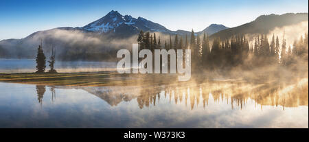 South Sister und Broken Top spiegeln sich in den ruhigen Gewässern des Sparks Lake bei Sonnenaufgang in der Cascades Range in Zentral-Oregon, USA, an einem frühen Morgen Stockfoto