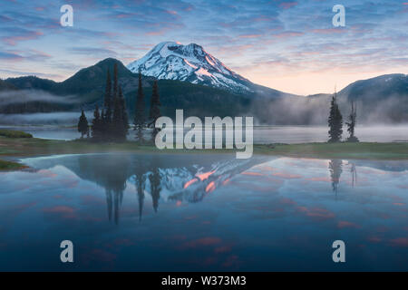 South Sister und Broken Top spiegeln sich in den ruhigen Gewässern des Sparks Lake bei Sonnenaufgang in der Cascades Range in Zentral-Oregon, USA, an einem frühen Morgen Stockfoto