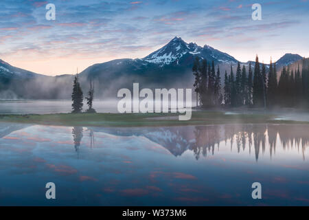 South Sister und Broken Top spiegeln sich in den ruhigen Gewässern des Sparks Lake bei Sonnenaufgang in der Cascades Range in Zentral-Oregon, USA, an einem frühen Morgen Stockfoto