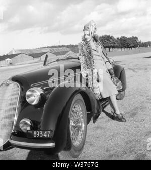 Damenmode in den 1940er Jahren. Eine junge Frau in einem typischen 40er Jahre Outfit. Einen passenden Rock und Jacke mit einem Leopard patterened Mantel hängt über ihre Schultern. Das Auto ist ein italienischer Sportwagen aus dem Autohersteller Alfa Romeo. Schweden 1946. Kristoffersson Ref X 1-5 Stockfoto