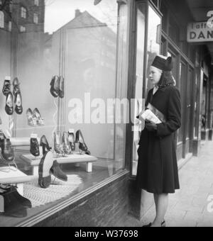 Window Shopping in den 1940er Jahren. Eine Frau steht vor einer Boutique zeigt die neuesten Mode in Damenschuhe. Sie trägt einen dunklen Mantel und einem dazu passenden modischen Hut. Schweden 1946. Kristoffersson AB 21-12 Stockfoto