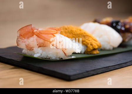 Detail der gedämpfte Garnelen nigiri, mit Hintergrund der Nigiri mit Pacific Seeigel, gedünsteter Lachs, gedämpfte Garnelen, Kaviar, gebratener Aal und Squid, Holz Stockfoto