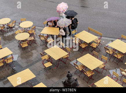 München, Deutschland. 13. Juli, 2019. Unter regenschirmen Passanten Verweilen im Regen auf einer verlassenen Straße Café im Zentrum der Stadt. Credit: Peter Kneffel/dpa/Alamy leben Nachrichten Stockfoto