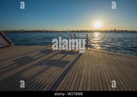 Metall Stahl Leitern auf der Rückseite Teak Deck eines großen Luxury Motor Yacht segeln auf einem tropischen Meer bei Sonnenuntergang Stockfoto