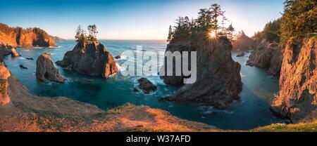 Sonnenuntergang im Samuel H. Boardman State Scenic Corridor, Oregon während einer goldenen Stunde Sonnenuntergang - Sonnenstrahlen durch Bäume mit dichter Vegetation. Wunderschönes Meer Stockfoto