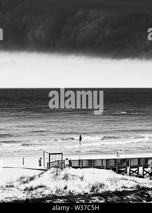 Gulf Shores, AL USA - 05/09/2019 - Sturmwolken über Strand und Holz- in B&W Gehweg Stockfoto