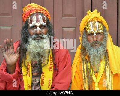 Zwei alte Nepalesische Vaishnavite sadhus (heilige Männer, die Anbetung Vishnu) mit bemalten Stirn tragen traditionelle rote und gelbe Outfit und für die Kamera posieren. Stockfoto