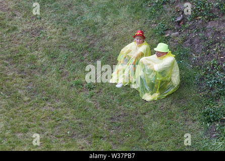 Hamburg, Deutschland. 13. Juli, 2019. Besucher des Schlagermoves sitzen mit raincaps auf einer Wiese an der Hellgoländer Allee. Quelle: Georg Wendt/dpa/Alamy leben Nachrichten Stockfoto