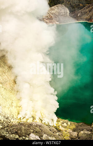 Krater eines Vulkans mit einem grünen Schwefelsäure See vulkanischen Ursprungs und vulkanische Rauch. Blick auf den rauchenden Vulkan Kawah Ijen in Indonesien Stockfoto