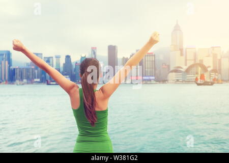 Glückliche Frau Erfolg jubeln von Hong Kong Skyline der Stadt mit ausgestreckten Arme angehoben. Erfolgreiche Sieger feiern Sonnenuntergang, Tsim Sha Tsui Promenade und Avenue der Stars in den Victoria Harbour und Kowloon. Stockfoto