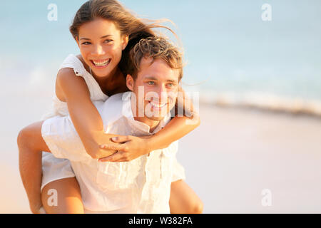 Verliebte Paare, die in Liebe Spaß-dating am Strand portrait. Schöne gesunde junge erwachsene Freundin Huckepack auf Freund umarmt glücklich. Multirassischen dating oder gesunde Beziehung Konzept. Stockfoto