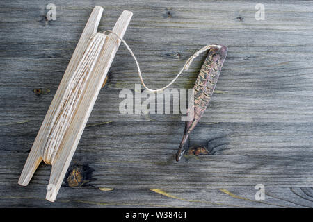 Alte Griff für vertikale blinken Raubfische. Kupfer geschmiedet Spinner und Haspel mit Seil auf Holz- rustikalen Hintergrund. Stockfoto