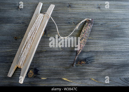 Alte Griff für vertikale blinken Raubfische. Kupfer geschmiedet Spinner und Haspel mit Seil auf Holz- rustikalen Hintergrund. Stockfoto