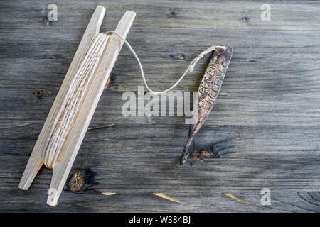 Alte Griff für vertikale blinken Raubfische. Kupfer geschmiedet Spinner und Haspel mit Seil auf Holz- rustikalen Hintergrund. Stockfoto