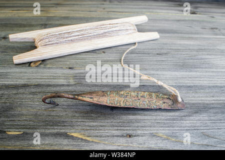 Alte Griff für vertikale blinken Raubfische. Kupfer geschmiedet Spinner und Haspel mit Seil auf Holz- rustikalen Hintergrund. Stockfoto