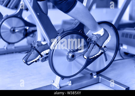 Heimtrainer mit durchdrehenden Rädern. Frau herausschneiden Radfahren in Fitnesscenter. closeup von Pedalen. Professionelle fitness center. Stockfoto