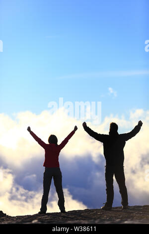 Glückliche Gewinner erreichen Leben Ziel - Erfolg Menschen am Gipfel. Business Achievement Konzept. Zwei Paar zusammen die Arme in die Luft des Glücks mit Vollendung in den Wolken bei Sonnenuntergang. Stockfoto