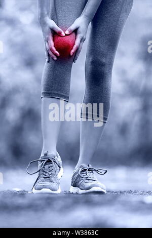Knieverletzung - Läufer mit Verstauchten bein Gelenkschmerzen. Nahaufnahme des Bein des weiblichen Athleten mit roter Kreis angezeigt. Woman Holding mit Händen um verletzten Knie im Sommer Natur Hintergrund. Stockfoto