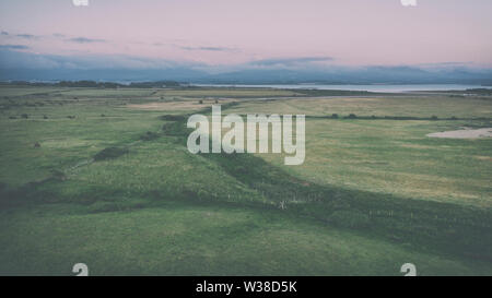 Luftaufnahme über Küsten Felder mit Berge in Wolken im Hintergrund begrenzt bei Sonnenuntergang in Anglesey, North Wales, UK Stockfoto