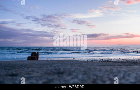 Sonnenuntergang Wolken über dem Meer, Blick von der Küste durch Holz- Wellenbrecher. Die Cardigan Bay in Pwllheli, North Wales, UK Stockfoto