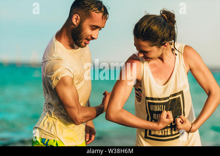 Junge fröhliche weibliche und männliche Schwimmer s flexing Biceps gegen blaue Meer Stockfoto