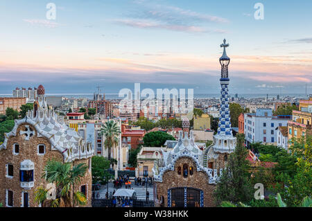 Auf Barcelona vom Park Güell auf den Sonnenuntergang. Im Vordergrund die bunten Gebäude vom Haupteingang. Barcelona, Spanien. Stockfoto