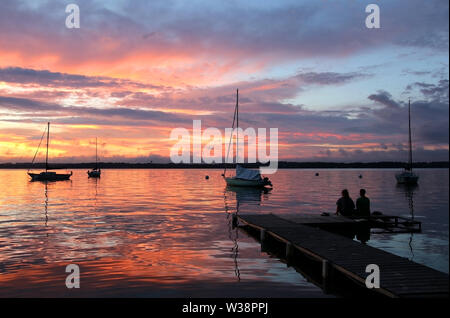 Super Sommer Abend Landschaft mit einer Gruppe von driften Yachten auf See, zwei Leute auf einem hölzernen Pier. Mendota bei spektakulären Sonnenuntergang. Hellen Himmel r Stockfoto