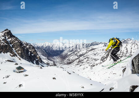 Skifahrer oben Snowbird Hütte und Gletscher springen einen Stein. Hinter ihm ist die Bartholf Creek Entwässerung und einem großen Couloir auf die fernen Gipfel. Stockfoto