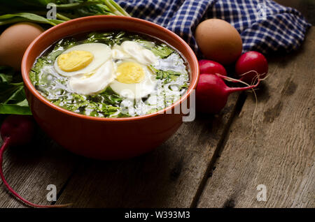 Grüner Borschtsch mit Sauerampfer, Spinat und Kartoffel, gekrönt mit gekochtem Ei und saure Sahne auf einem alten Holztisch. Essen Foto im rustikalen Stil. Stockfoto