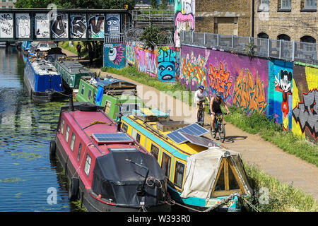 Radfahrer passieren Graffiti beim Radfahren entlang Kanal in Hackney, London England Vereinigtes Königreich Großbritannien Stockfoto