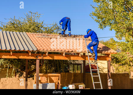 Zwei Schüler bereiten ein Dach Solarzellen mit einer Metallschiene oben Dachziegel, auf ein Gebäude der Schule in Otjiwarongo, Namibia zu installieren. Stockfoto