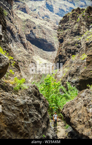 Junge Reisende bleibt an der Spitze der riesigen Felsbrocken in die Masca Schlucht, Teneriffa, mit erstarrter Lava Flow Schichten und arch Bildung. Schlucht Stockfoto