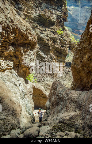 Junge Reisende bleibt an der Spitze der riesigen Felsbrocken in die Masca Schlucht, Teneriffa, mit erstarrter Lava Flow Schichten und arch Bildung. Schlucht Stockfoto