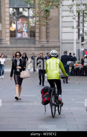 Eine Frau mit Helm und einem gelben Regenmantel reitet ihr Fahrrad mit einem seitlichen Satchel durch Sydneys Martin Place an einem Wochentag morgens Stockfoto