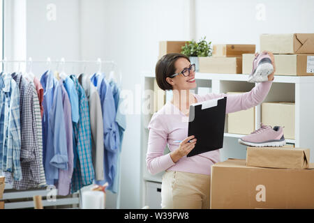 Glückliche junge Arbeitnehmer, der online Shop mit dem Dokument auf Paar niedliche rosa Sneakers während der Arbeit Stockfoto