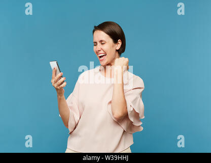 Junge ekstatisch weiblichen Blick auf Bildschirm des Smartphones beim Ausdrücken der Freude in der Isolation Stockfoto