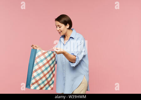 Junge aufgeregt weiblich in casualwear auf Überraschung in offenen paperbag Während posieren in Isolation Stockfoto