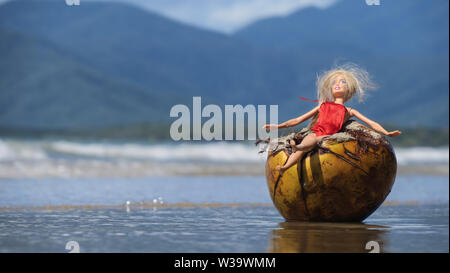 Australischen Strand Szenen. Das Leben ist ein Strand in Australien, eine Barbie Puppe entspannt in einer Kokosnuss am Four Mile Beach im Norden von Queensland. Stockfoto