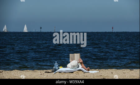 Australischen Strand Szenen. Das Leben ist ein Strand in Australien, vor allem mit einem guten Buch an einem sonnigen Tag durch die Wasser der Bucht von Port Phillip, Melbourne, Australien. Stockfoto