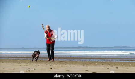 Eine alte Dame schlug den Tennisball zu ihrem Hund am Strand. Stockfoto