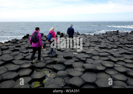 Drei Besucher auf der Oberseite des Schwarzen sechseckigen Basaltsäulen Verriegelung auf Causeway Coastal Weg des Riesen, County Antrim, Nordirland, Großbritannien. Stockfoto