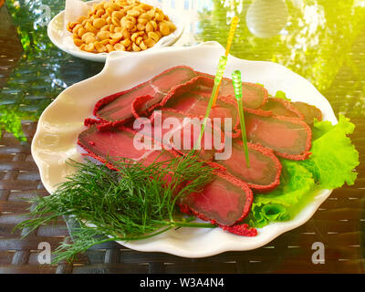 Köstliche frische basturma auf einem Teller mit Salat und Erdnüsse in einem weißen Untertasse. Tabelle im Sommer bar. Soft Focus Stockfoto