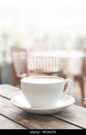 Eine weiße Tasse steht auf einem hölzernen Tisch in einem Coffee Shop. leicht verschwommenen Hintergrund. Bis zu schließen, vertikale Foto Stockfoto