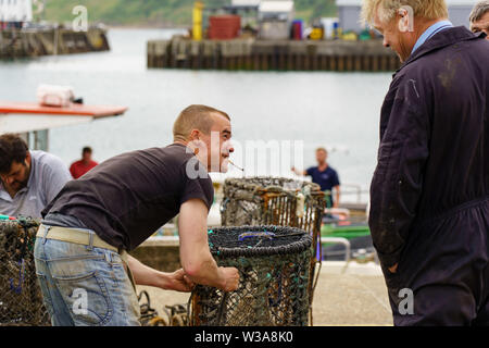 Fischer rauchen eine Zigarette, während sie Hummer-Töpfe an einer Hafenpromenade in Scarborough, North Yorkshire, England, Großbritannien reparieren. Stockfoto