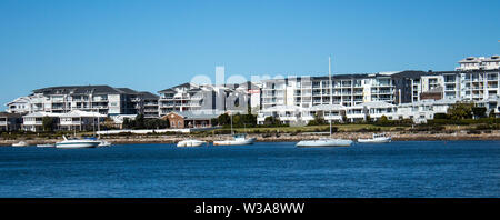 Großes Apartment am Wasser Häuser, Eigentumswohnungen in suburban Gemeinschaft am Flussufer mit Boote auf dem Wasser, blauer Himmel im Hintergrund Stockfoto