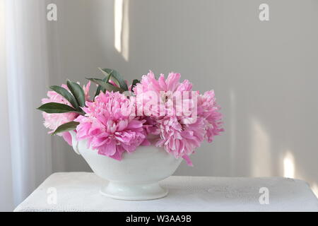 Rosa pfingstrose Blüten in einer weißen Schüssel auf einem weißen Tisch. Weißer Hintergrund. Immer noch leben. Licht am Morgen Licht im Innen weiss. Stockfoto