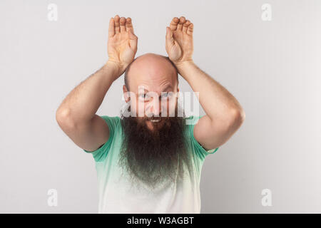 Portrait von Lustig verrückt Kahl im mittleren Alter Mann mit langem Bart in hellem Grün t-shirt mit Hasenohren Geste und Kamera. indoor Stu Stockfoto