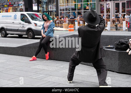 Ein Fotograf in einem zoot Suit und Fedora macht ein Foto von einer schönen asiatischen Frau mit grünen Haaren. Am Times Square, Manhattan, New York City. Stockfoto